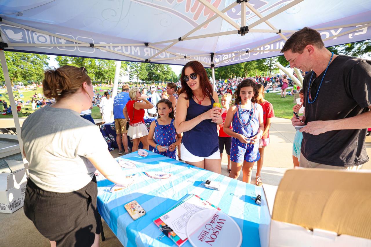 People talk at one of the sponsors tables under a tent at the concerts.